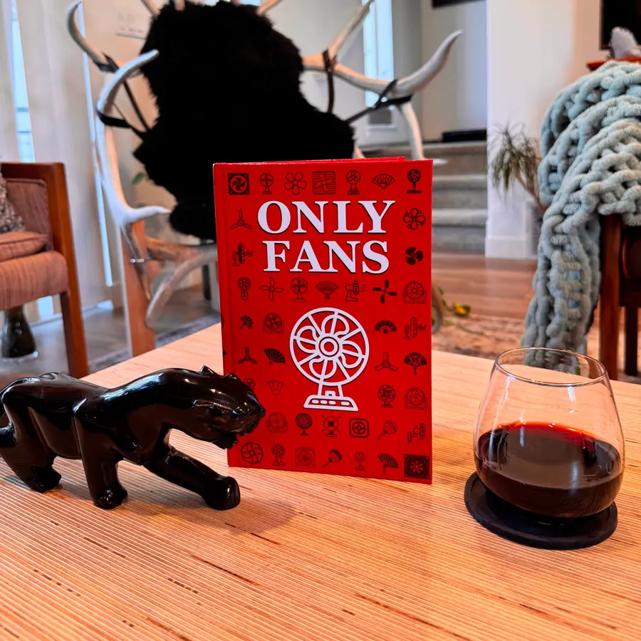 Only Fans standing on a coffee table beside a glass of red wine and a black ceramic panther.